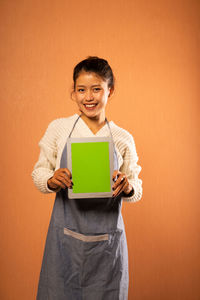 Portrait of young woman holding box against yellow background