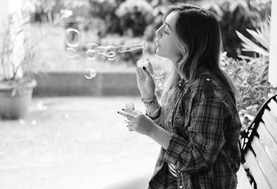 Woman blowing bubble while sitting on bench