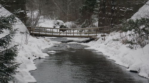 Snow covered footbridge over stream during winter