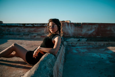 Young woman sitting on sunglasses against clear sky