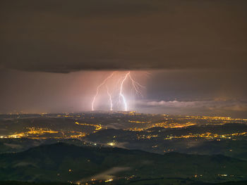 Lightning over illuminated city against sky at night