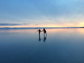 Silhouette children ice skating against sky during sunset