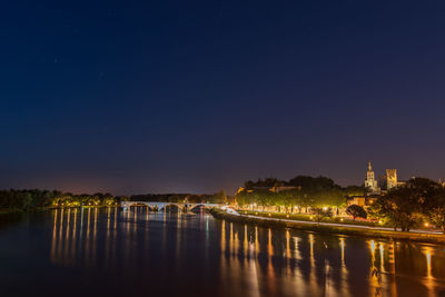 Illuminated buildings by river against sky at night