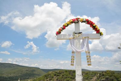 Flowers and fabric decorated on cross against mountains