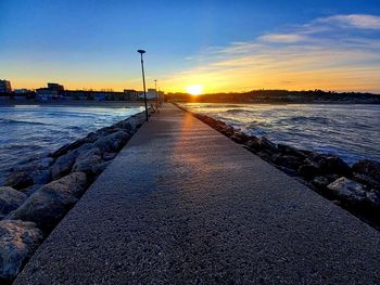 Surface level of road by sea against sky during sunset