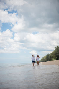 Man and woman walking at beach against sky