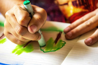 Child hands drawing with crayon on a sheet of paper illuminated by the side light from the window