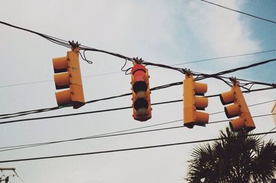 Low angle view of electric lamp hanging against sky