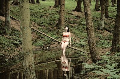 Woman in bikini sitting on fallen tree trunk over pond at forest