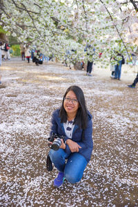 Portrait of smiling woman crouching by flowering tree at park