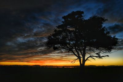 Silhouette of trees on landscape against cloudy sky