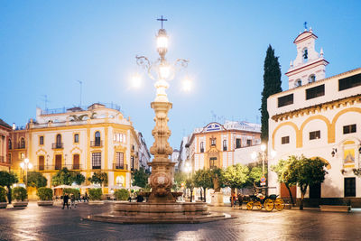 Illuminated street light and buildings against clear blue sky