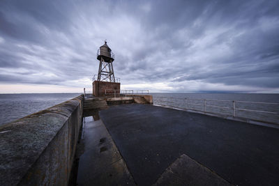 Lighthouse on pier by sea against sky