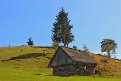 House and trees on field against clear blue sky