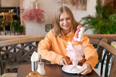 Happy woman eating sweet dessert in form pink flamingo in restaurant, woman