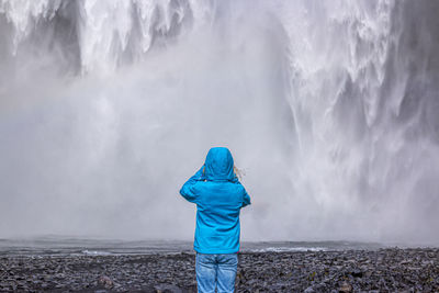 Rear view of person standing against waterfall