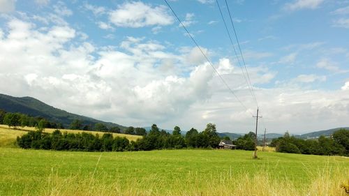 Electricity pylon on field against cloudy sky