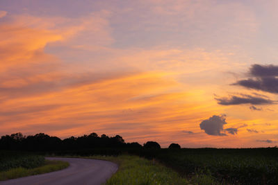 Road amidst field against sky during sunset