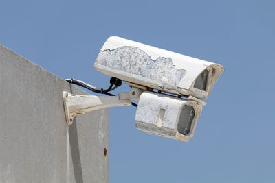 Low angle view of security camera against clear blue sky