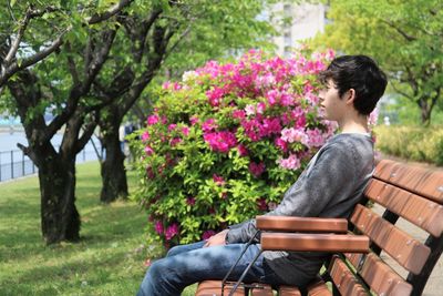 Teenage boy sitting on bench in park by flowering azaleas