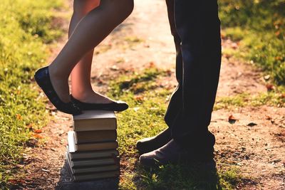 Low section of girlfriend standing on stacked books while boyfriend at field