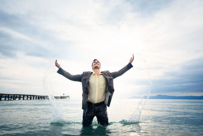 Full length of young man standing in sea against sky