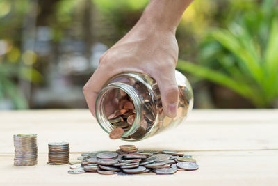 Cropped hand holding jar with coins over table