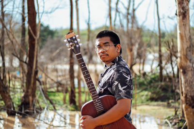 Portrait of young man holding guitar standing in park