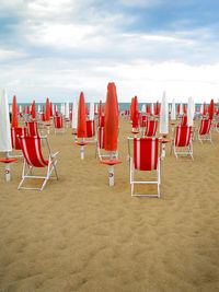 Closed parasols with chairs on sand at beach against sky