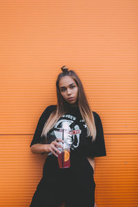 Portrait of young woman drinking glass against orange wall