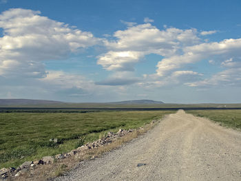 Dirt road amidst field against sky