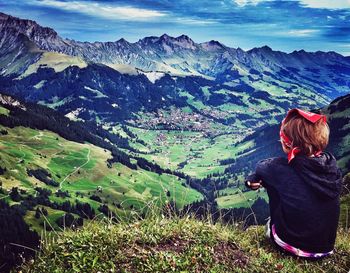 Boy sitting on mountain against sky