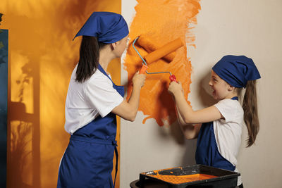 Rear view of female friends standing against yellow wall