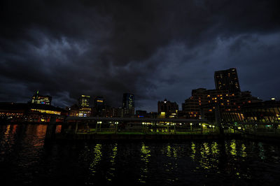 Illuminated city by river against sky at night