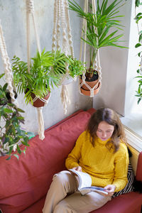 Woman sitting on sofa against potted plants