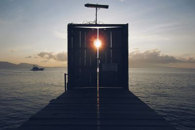 Closed door on pier at sea against sky during sunset