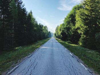 Empty road amidst trees in forest against sky