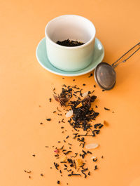 'tea preparing ceremony,  cup, tea strainer and black fruit herbal dry tea on orange background. '