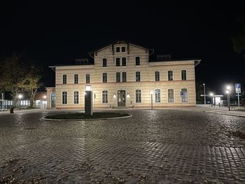 Illuminated building by street against sky at night