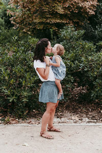 Mother and daughter kissing each other while standing in public park