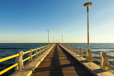 Empty street leading towards sea against clear sky