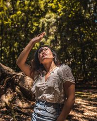 Young woman looking up while standing by tree in forest