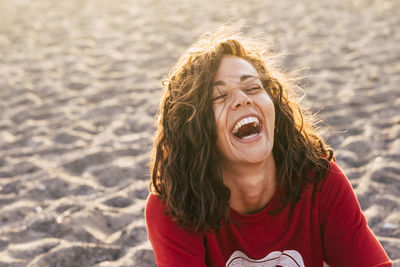 High angle view of happy young woman laughing while sitting at beach