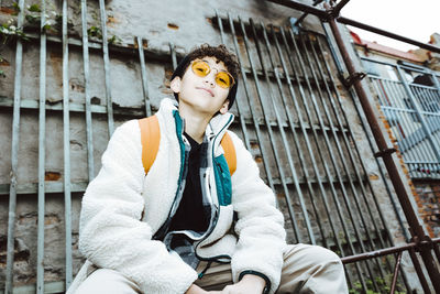 Portrait of boy wearing sunglasses sitting on railing against wall