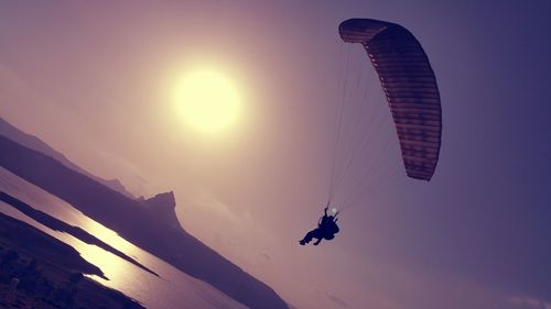 Low angle view of silhouette people paragliding against sky during sunset