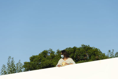 Low angle view of person sitting against clear blue sky