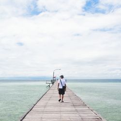 Rear view of man walking on pier at sea against sky