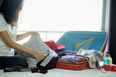 Woman packing bag while sitting on bed in bedroom