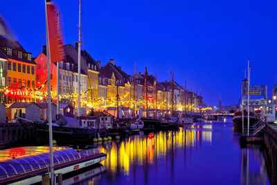 Boats moored in canal against illuminated buildings at dusk