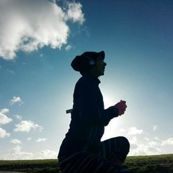 Silhouette man sitting on field against sky